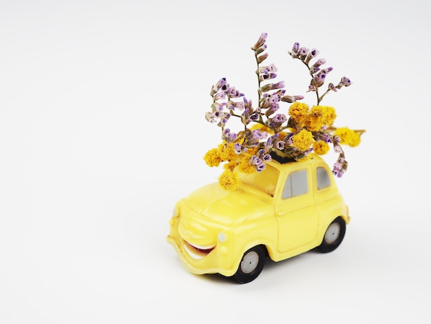 Petite voiture jouet jaune avec un bouquet de fleurs sauvages sur fond blanc.