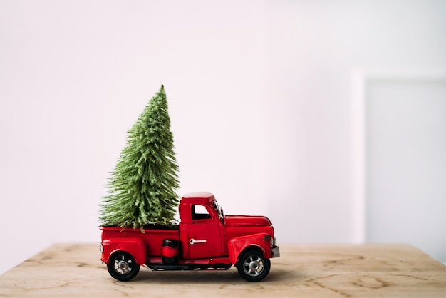 Petite voiture jouet rouge avec arbre de Noël vert sur fond en bois et blanc debout près du mur.