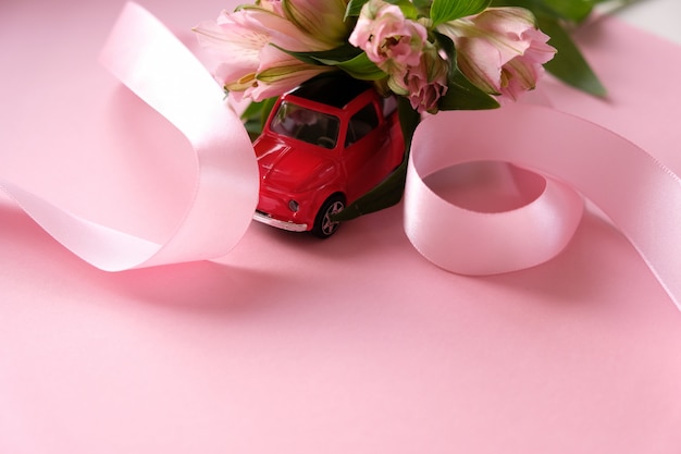 Petite voiture jouet rouge porte un bouquet de fleurs roses