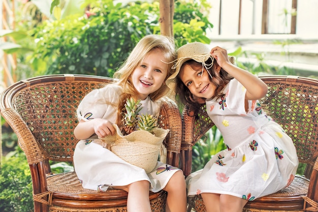 Petites belles filles mignonnes enfants en robes blanches avec des ananas dans les mains sur des plantes tropicales