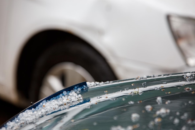 Petites boules de glace de grêle sur le capot de la voiture verte après une forte tempête estivale