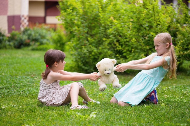 Petites copines de jolies filles assises sur la pelouse et se querellent pour des jouets
