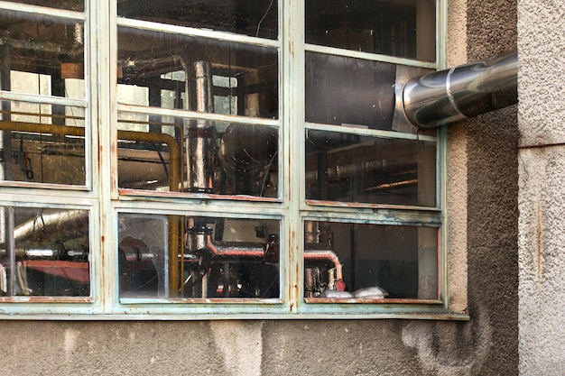 Petites fenêtres anciennes de l'installation de chauffage de l'extérieur. Caloducs recouverts d'une feuille d'argent visible derrière une vitre.