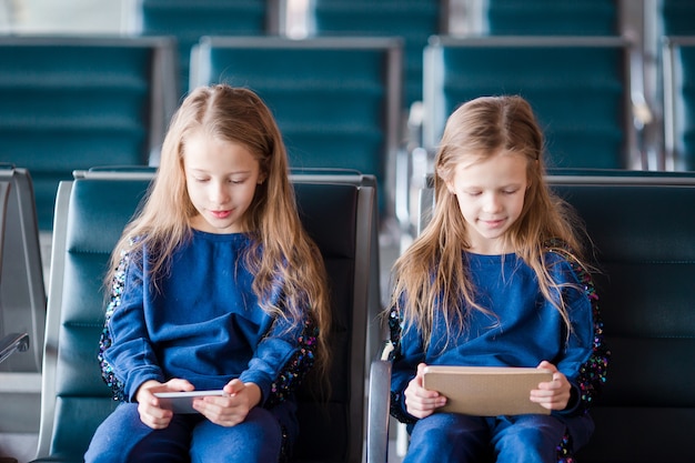 Petites filles adorables à l'aéroport en attente d'embarquement jouant avec un ordinateur portable