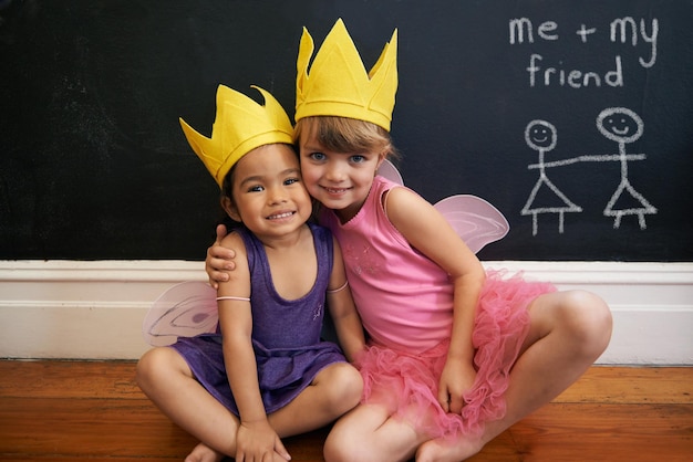 Petites filles amies et portrait avec étreindre couronne et sourire pour l'amour et le bonheur enfants jeunesse et câlin pour le visage plaisir et l'attachement avec tableau noir et costume de princesse féerie pour s'habiller