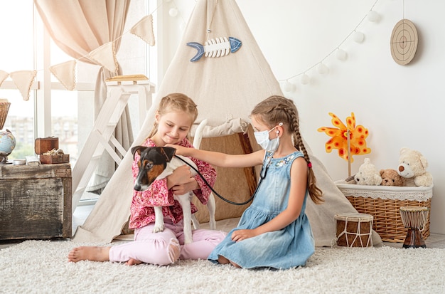 Petites filles avec chien écoute phonendoscope comme médecin assis sur le sol dans la salle de jeux