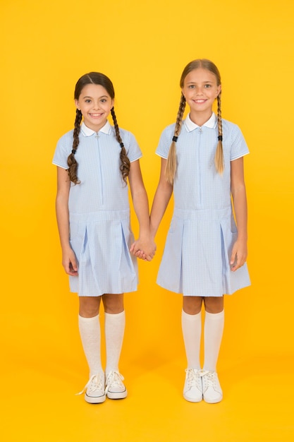 Petites filles collées en uniforme scolaire rétro regardent les enfants dans le style vintage vieille école enfant mode amis heureux sur fond jaune mode beauté enfance bonheur concept de fraternité