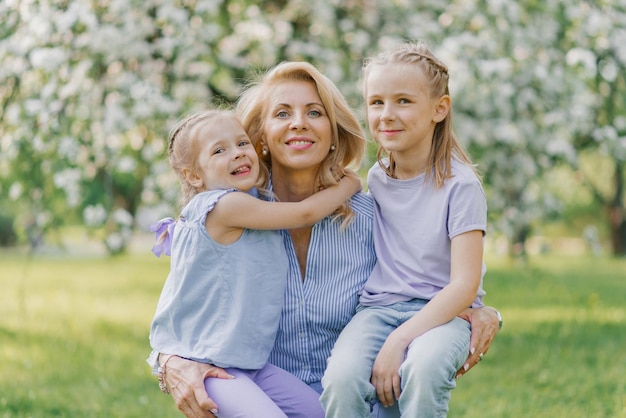 Les petites-filles embrassent leur grand-mère au printemps dans un jardin fleuri à l'extérieur