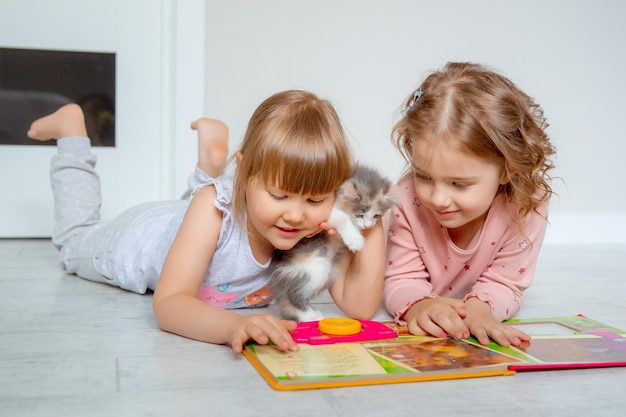 Petites filles enfants jouant avec un chaton lisant un livre à la maison sur le sol