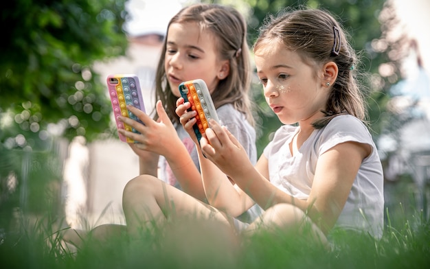 Petites filles à l'extérieur avec des téléphones dans un étui à boutons, un jouet anti-stress tendance.