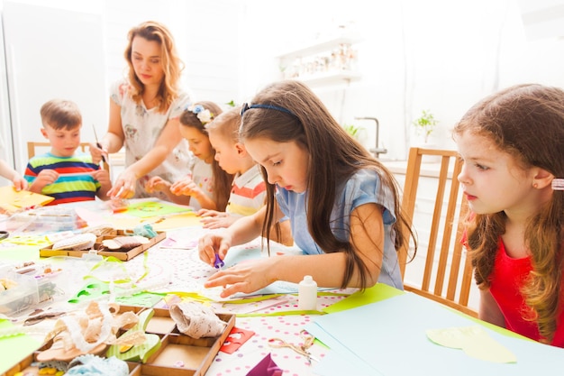 Les petites filles et les garçons font des cartes postales avec l'aide d'un enseignant