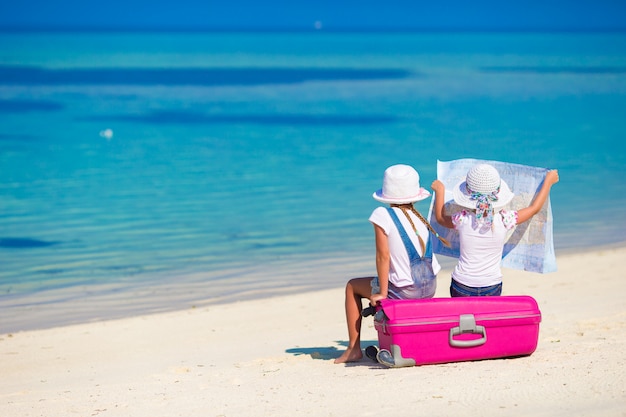 Petites filles avec une grosse valise et une carte sur une plage tropicale
