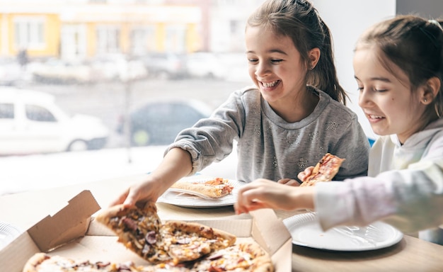 Les petites filles heureuses mangent de la pizza dans un café