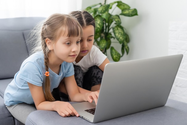 Petites filles à la maison avec ordinateur portable, chat vidéo avec leurs amis.