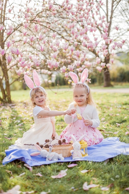 De petites filles mignonnes sont assises sur l'herbe près de la mogolie. Filles en costumes de lapins de Pâques. Printemps.