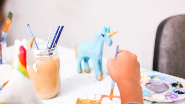 Petites filles peignant une licorne en papier mâché avec de la peinture acrylique.