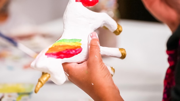 Petites filles peignant une licorne en papier mâché avec de la peinture acrylique.