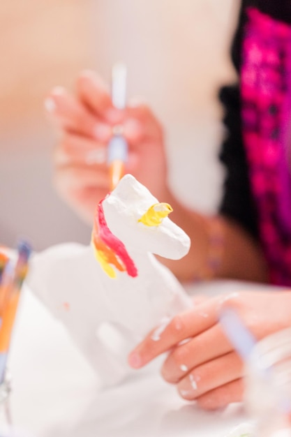 Petites filles peignant une licorne en papier mâché avec de la peinture acrylique.