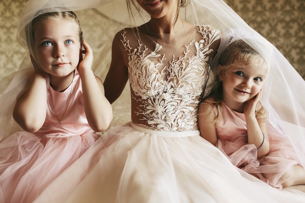 Les petites filles en robes roses sont cachées sous le voile de la mariée