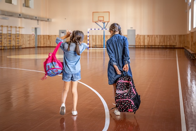 Petites filles avec des sacs à dos dans un gymnase d'école vide.