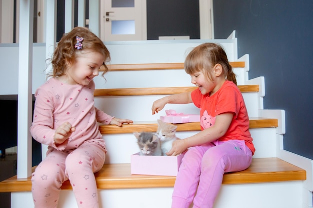 Les petites filles sont assises à la maison dans les escaliers et jouent avec un chaton