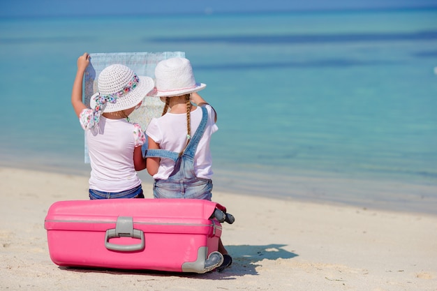 Petites filles de touristes avec une grosse valise sur une plage blanche tropicale