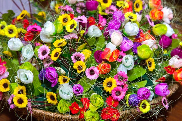 Petites fleurs artificielles multicolores colorées de fond dans un panier