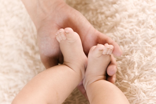 Petites jambes de bébé nues dans les mains de maman
