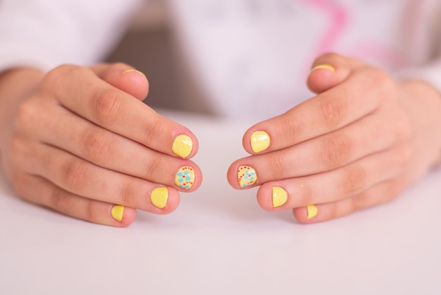 Petites mains de fille avec de beaux ongles de manucure conception de fleur de vernis jaune de gel