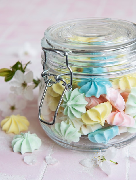 Petites meringues colorées dans le bocal en verre sur fond de tuile rose