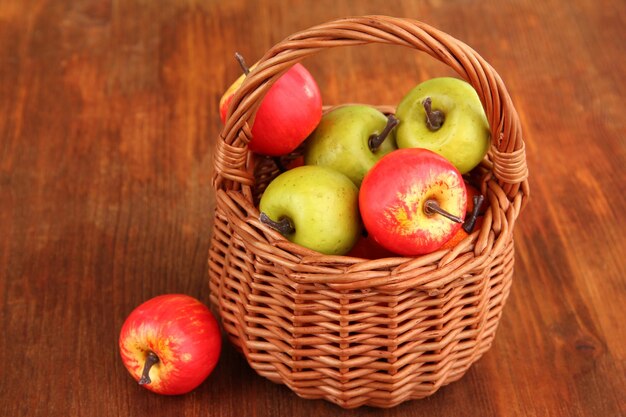 Petites pommes dans un panier en osier sur fond de bois
