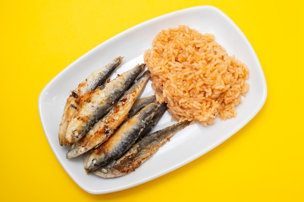 Petites sardines frites avec riz tomate sur plat blanc sur fond jaune