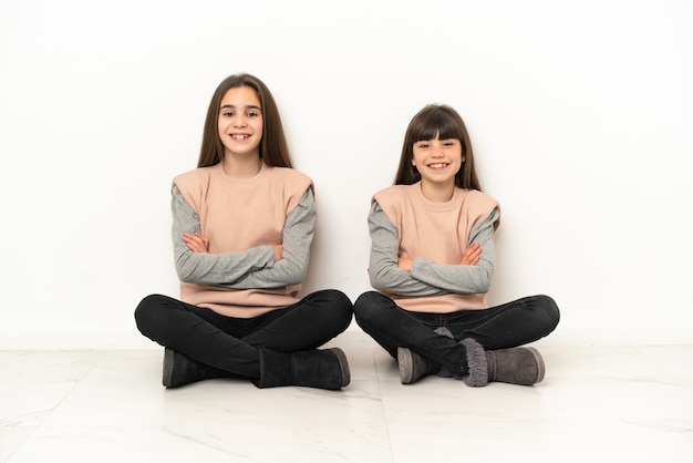 Petites sœurs assis sur le sol isolé sur fond blanc en gardant les bras croisés en position frontale