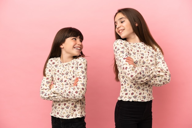 Petites soeurs filles isolées sur fond rose regardant par-dessus l'épaule avec un sourire