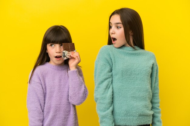 Petites Soeurs Isolées Sur Fond Jaune Prenant Une Tablette De Chocolat Et Surprises