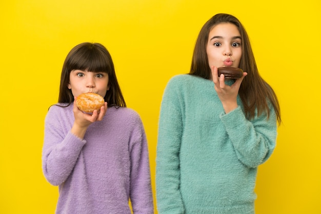 Petites sœurs isolées sur fond jaune tenant un beignet