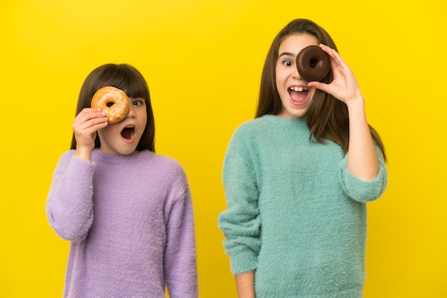 Petites soeurs isolées sur fond jaune tenant des beignets dans un oeil