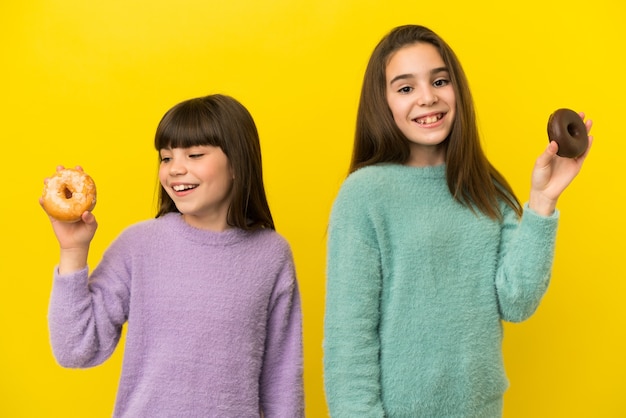 Petites soeurs isolées sur fond jaune tenant des beignets avec une expression heureuse