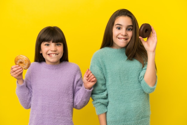 Petites sœurs isolées sur fond jaune tenant des beignets