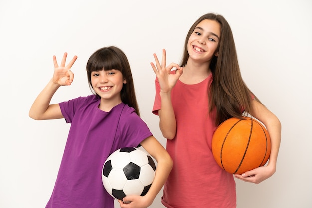 Petites sœurs jouant au football et au basket-ball isolé sur fond blanc montrant un signe ok avec les doigts