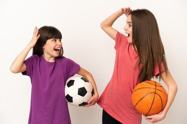 Petites soeurs jouant au football et au basket-ball isolées sur fond blanc avec une expression faciale surprise et choquée