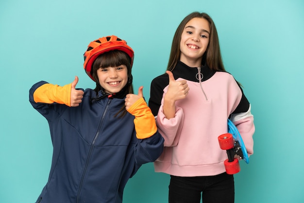 Petites sœurs pratiquant le cyclisme et patineur isolé sur fond bleu donnant un geste de pouce en l'air avec les deux mains et souriant