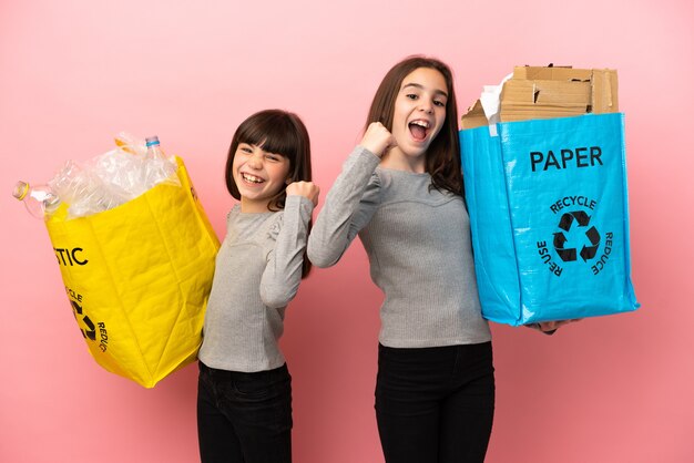 Petites sœurs recyclage du papier et du plastique isolé sur fond rose célébrant une victoire