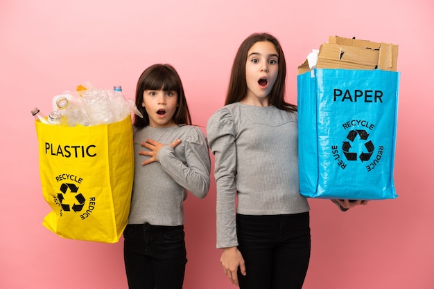 Petites sœurs recyclage du papier et du plastique isolé sur fond rose avec surprise et expression faciale choquée
