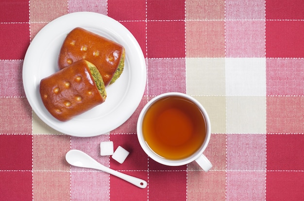 De petites tartes aux légumes verts et aux légumes et une tasse de thé sont situées sur une table avec une nappe rouge, vue de dessus