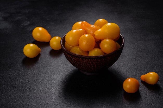 Petites tomates jaunes en forme de poire dans une assiette en céramique sur une table en béton foncé