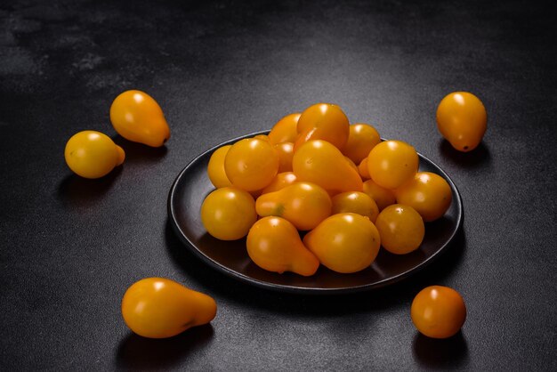 Petites tomates jaunes en forme de poire dans une assiette en céramique sur une table en béton foncé