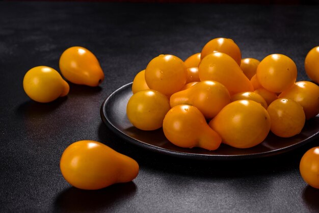 Petites tomates jaunes en forme de poire dans une assiette en céramique sur une table en béton foncé