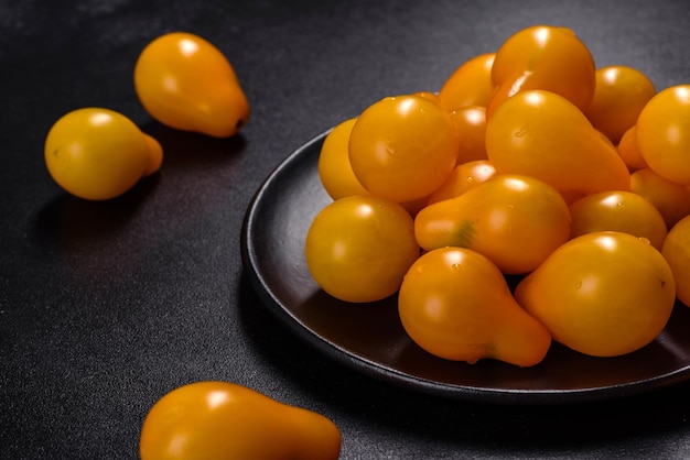 Petites tomates jaunes en forme de poire dans une assiette en céramique sur une table en béton foncé