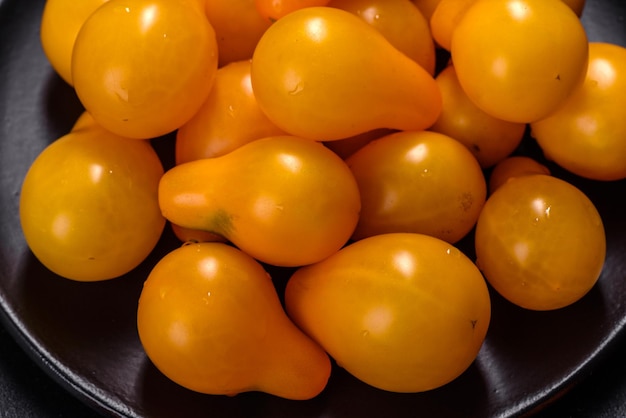 Petites tomates jaunes en forme de poire dans une assiette en céramique sur une table en béton foncé